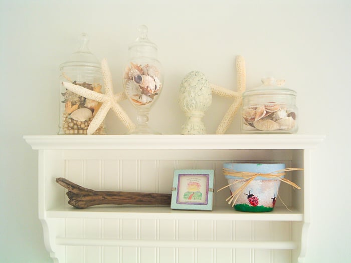 White shelf in a beach themed bathroom with starfish and seashells.