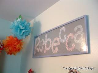 Framed name art with hanging pom poms.