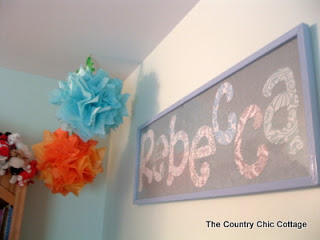 Framed name art with orange and blue tissue paper pom pom.