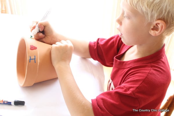 a child using a marker to paint a flower pot