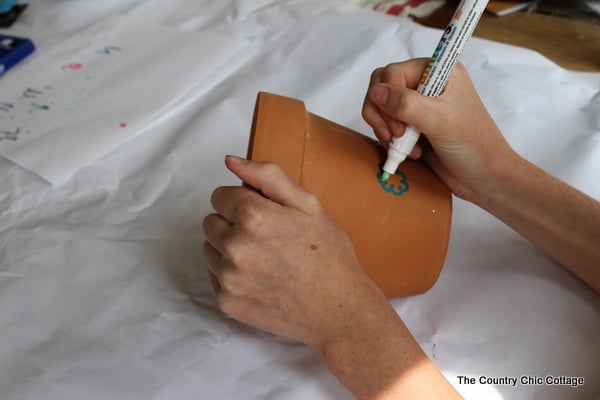 someone using a paint marker to decorate a flower pot