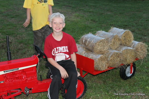 Blonde son sitting on pedal tractor with attached trailer.