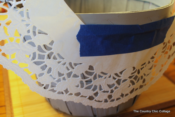 taping a paper doily on a basket with masking tape