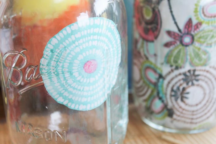 Using decoupage to adhere floral fabric cutouts to the inside of a mason jar