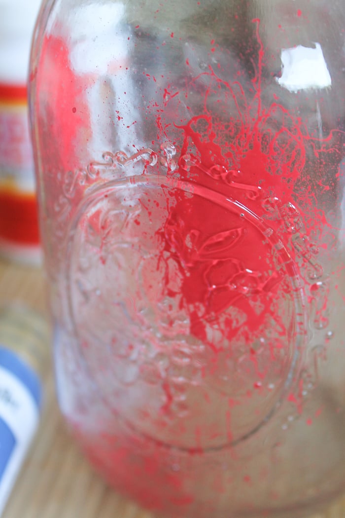 Using a splatter paint technique to paint the inside of a mason jar with red paint