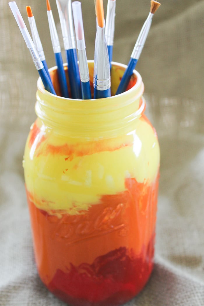 This vibrant sunset painted mason jar is perfect for holding crafting supplies like paint brushes
