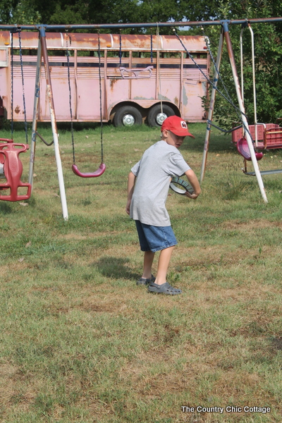 boy with red hat throwing paper frisbee in front of swing set