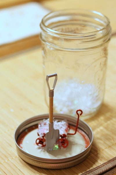 Hot gluing a miniature shovel to the lid of a mason jar. 