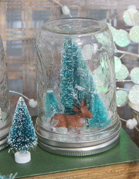 DIY Waterless Snow Globes with Kids A reindeer and Christmas trees inside of a homemade snow globe.