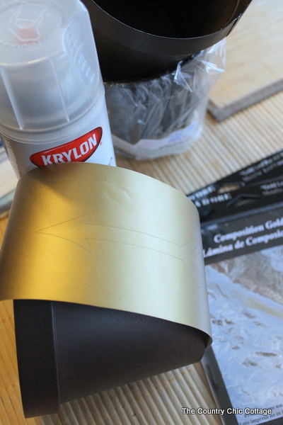 Add a gold leaf touch to metal flower pots with this easy to follow tutorial. Gold leaf is easy to use and makes a bold statement. Using gold vinyl to create a mask to apply to the metal flower pot.