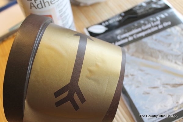Add a gold leaf touch to metal flower pots with this easy to follow tutorial. Gold leaf is easy to use and makes a bold statement. Applying vinyl to metal flower pot.