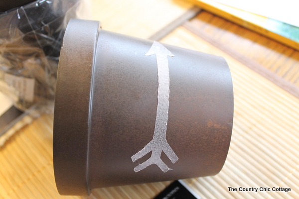 Add a gold leaf touch to metal flower pots with this easy to follow tutorial. Gold leaf is easy to use and makes a bold statement. Arrow design on metal flower pot with spray adhesive.