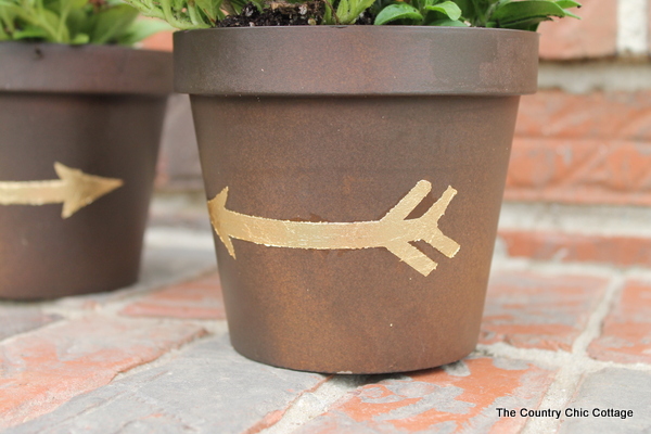 Add a gold leaf touch to metal flower pots with this easy to follow tutorial. Gold leaf is easy to use and makes a bold statement. Finished gold leaf metal flower pot with gold arrow design.