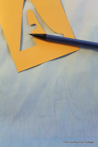 Using a stencil to trace a letter onto a fabric tote. 