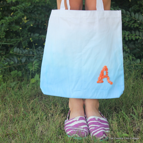 A great button monogram tote for back to school. Perfect for the student, teacher, or a special gift for mom to carry herself. Make your own ombre tote in a few simple steps. Woman holding a DIY monogram tote bag,