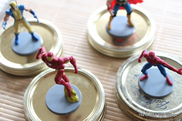 superhero figures being glued to jar lids