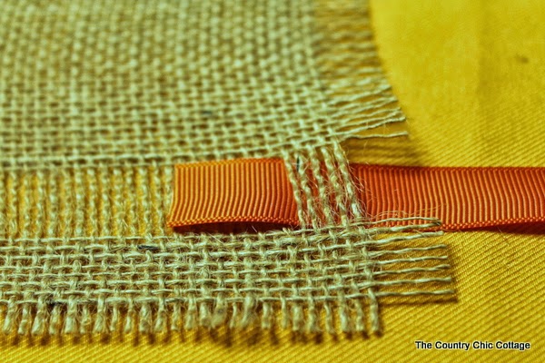 DIY Burlap Thankful Place Mats -- the perfect place mats to make for your Thanksgiving feast. Super simple to make and you can use the word "thankful" or the word of your choice. ribbon going through burlap