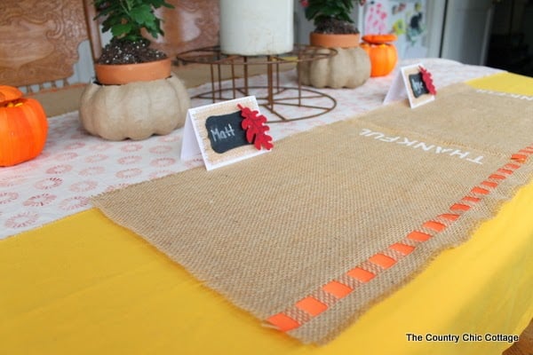 DIY Burlap Thankful Place Mats -- the perfect place mats to make for your Thanksgiving feast. Super simple to make and you can use the word "thankful" or the word of your choice. two fall placemats on yellow cloth for table