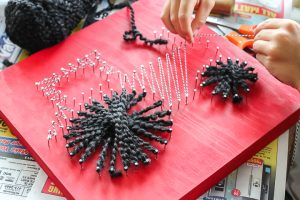 kid wrapping string around nails for string art