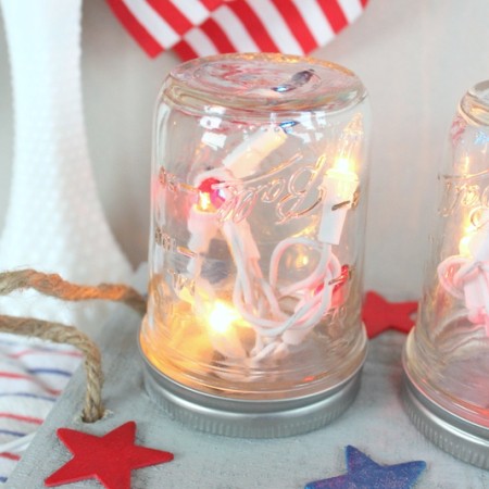 Patriotic Mason Jar Centerpiece for the Fourth of July -- make this centerpiece and light up your party in style! A fun way to add string lights to your table in mason jars! Easy to make by following this craft tutorial.