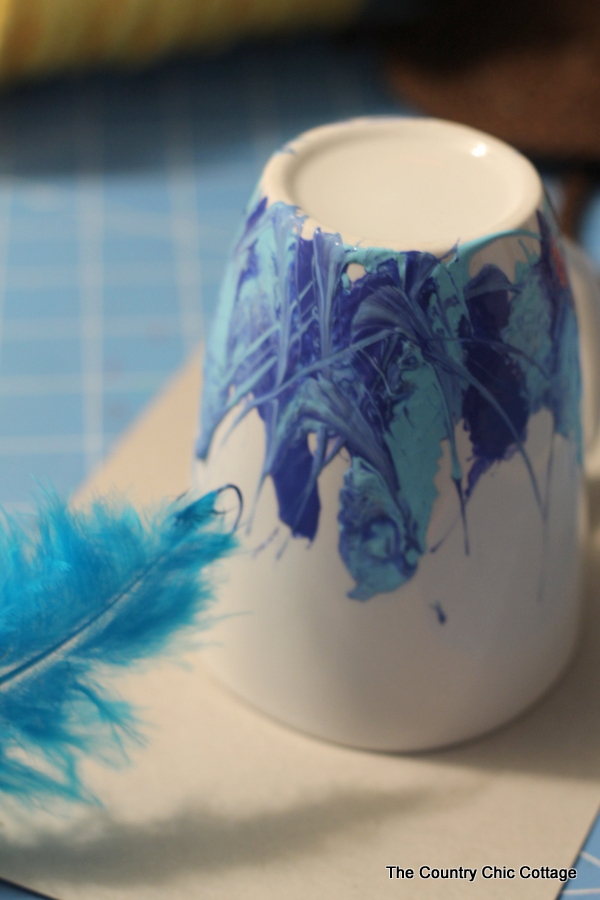 Use a feather to blend blue paint on a white coffee mug