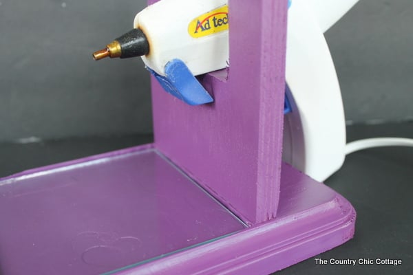 Finished DIY purple hot glue gun holder, white hot glue gun resting in stand, on dark gray background