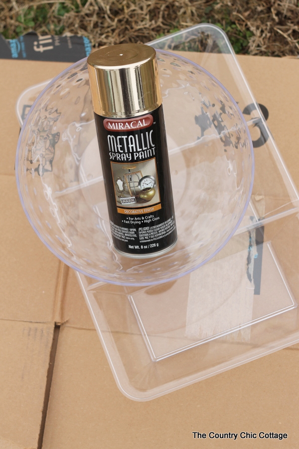 can of gold metallic spray paint and two plastic organizers on a piece of cardboard preparing to spray paint