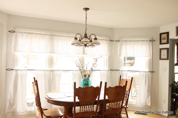 kitchen table decorated with rustic kitchen decor pieces and windows with farmhouse curtains and rods