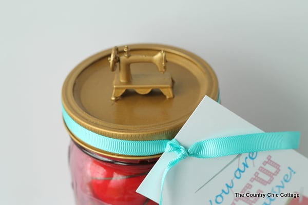 a mason jar sewing kit topped with a gold, miniature sewing machine