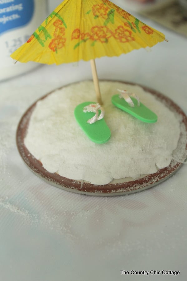Miniature umbrella and beach flip flops on top of clay in a mason jar