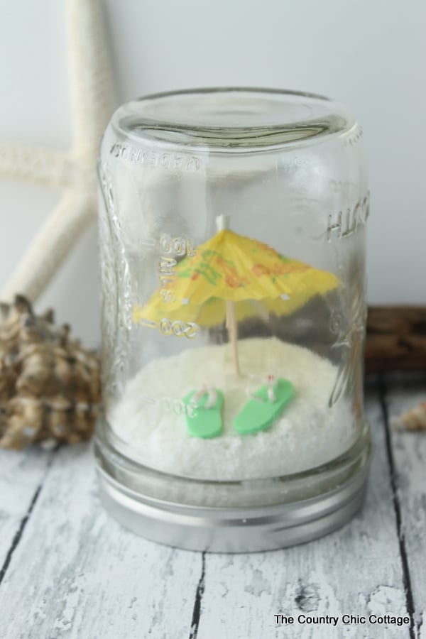 Miniature umbrella and flip flops on fake sand inside a mason jar