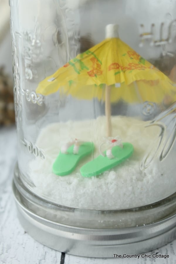 Close up angle of mini umbrella and flip flops inside a beach mason jar