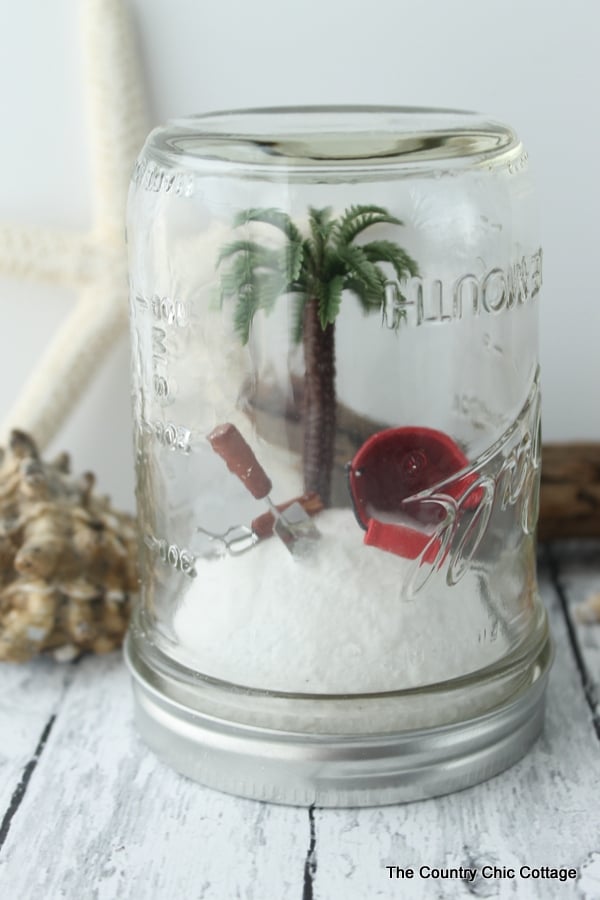A beach mason jar filled with fake sand, a mini palm tree, and mini shovels and buckets.