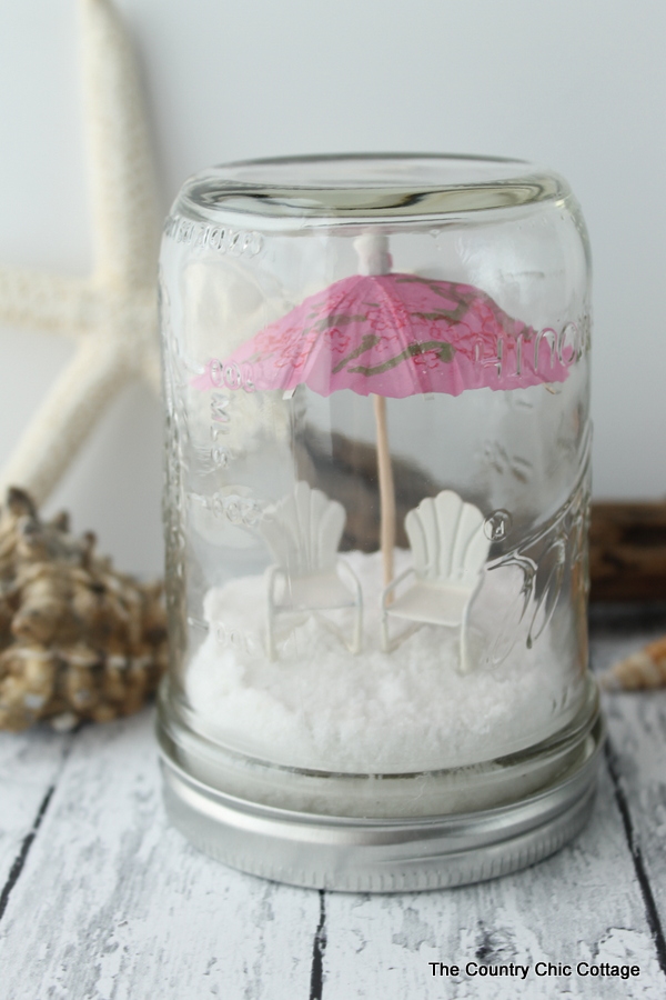 Miniature pink beach umbrella with two lounge chairs beneath it in the mason jar.