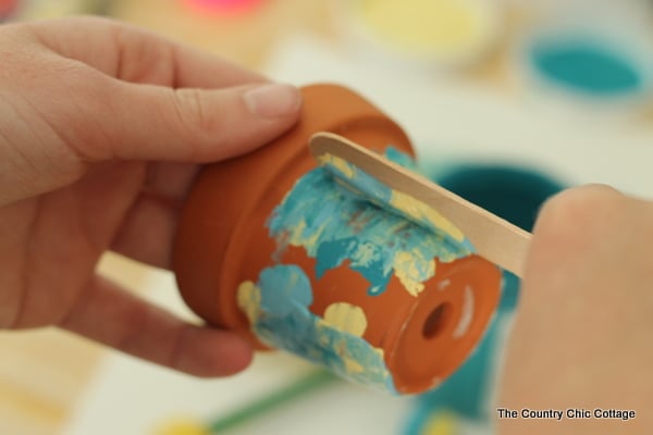 Smearing paint on a small terra cotta pot for marbled look