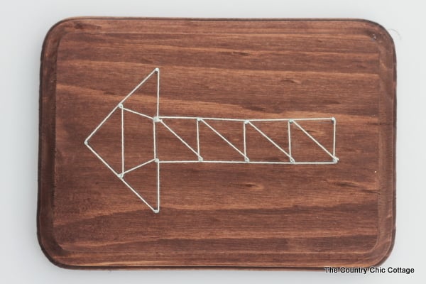 Geometric string art arrow made with nails and white string.