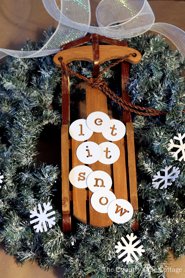 christmas wreath with sleigh attached in center and "let it snow" message on sleigh