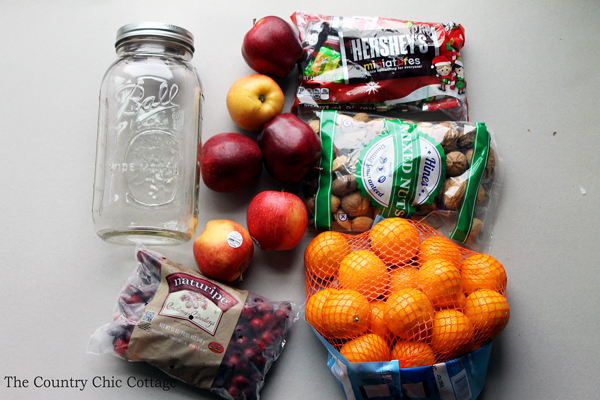 supplies needed for fruit basket in a jar, including apples, nuts, chocolates, oranges, cranberries, and a jar