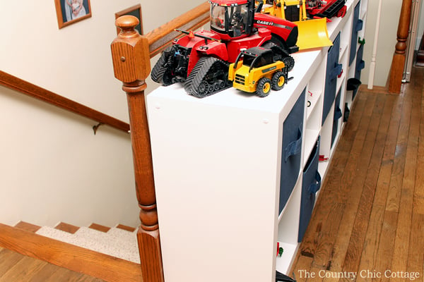 white cube organizer with tractor toys on top alongside stair railing