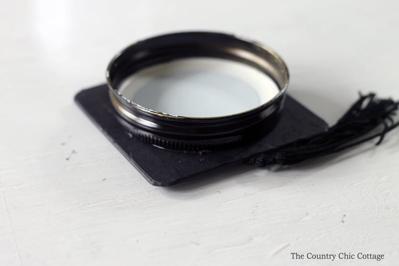 Attach the mason jar lid to the graduation cap using hot glue