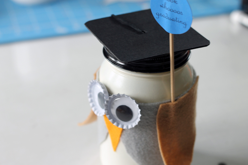 hot glue the owl wings to the mason jar. making sure to attach the graduation sign under a wing