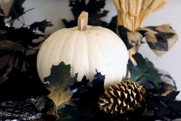 white pumpkin with black and gold leaves and pinecones