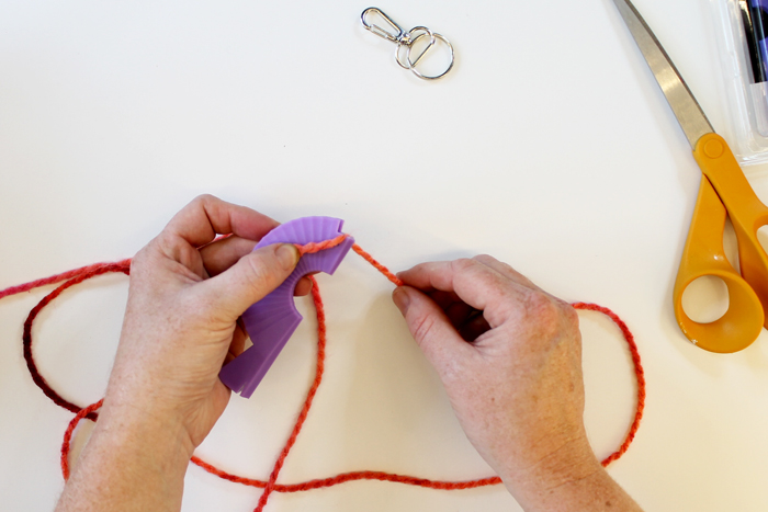 top shot of person wrapping pink yarn around small purple loom