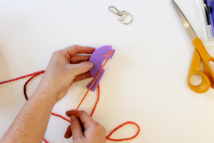 top shot of person wrapping pink yarn around small purple loom