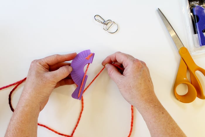 top shot of person wrapping pink yarn around small purple loom