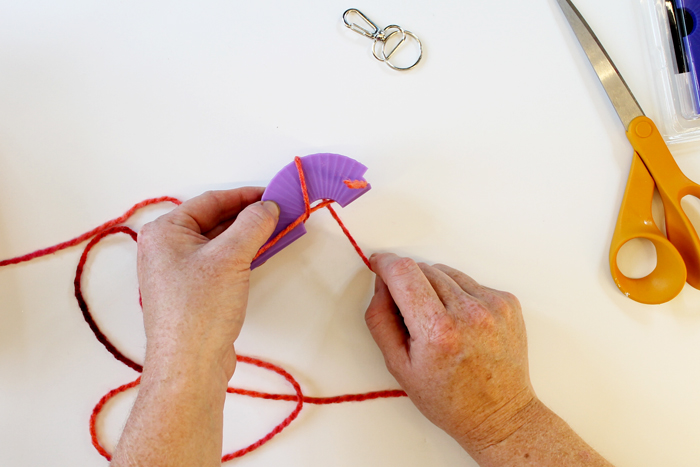 top shot of person wrapping pink yarn around small purple loom