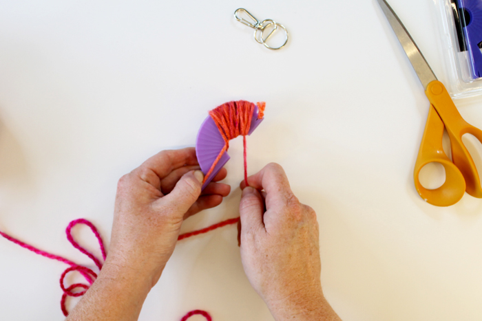 top shot of person wrapping pink yarn around small purple loom