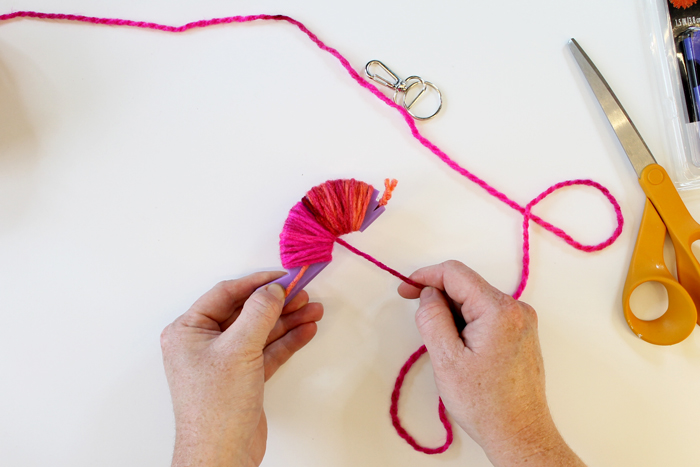 top shot of person wrapping pink yarn around small purple loom