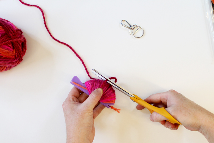 person wrapping pink yarn around small purple pom pom loom