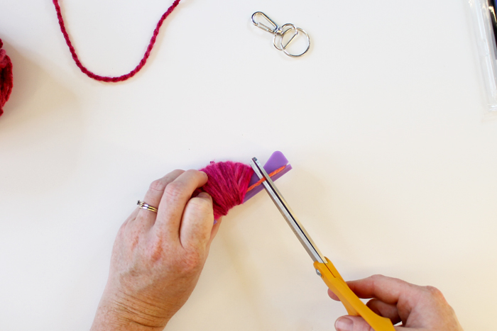 person wrapping pink yarn around small purple pom pom loom